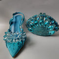 Turquoise high-heeled shoe with floral embellishments and matching clutch on a gray background, Obroi