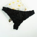 Black thong on a white surface with a floral magazine underneath, Obroi