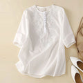 White embroidered blouse on a beige background with white shoes and a beige handbag, Obroi