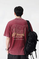 Person wearing a maroon t-shirt with motivational text on the back, standing against a white background, Obroi