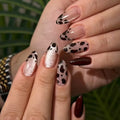 Close-up of a hand with decorative nail art against a blurred green background, Obroi