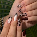 Close-up of a hand with decorative nail art against a blurred green background, Obroi
