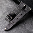 Black leather watch strap with gold accents on a dark surface, Obroi