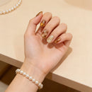 Hand with glittery nail polish wearing a pearl bracelet on a beige background, Obroi