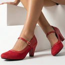 Red high-heeled shoes worn by a person sitting on a white surface, Obroi
