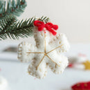White felt snowflake ornament with gold accents and a red ribbon on a blurred Christmas tree branch , Obroi