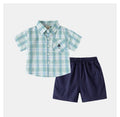 A toddler boy's two-piece clothing set featuring a short-sleeve button-down shirt in a light green and white plaid pattern with a chest pocket, paired with navy blue elastic-waist shorts, shown on a light gray background, Obroi