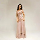 A woman modeling a long, sleeveless pink gown with intricate lace and beadwork on a plain light gray studio background. The brand name 'Obroi' is printed in black at the top left.