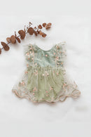 A sleeveless baby dress in pale mint green tulle with pink floral embroidery and pearl-like bead trim, laid flat on a white background with dried brown leaves in the corner, Obroi