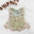 A sleeveless baby dress in pale mint green tulle with pink floral embroidery and pearl-like trim, laid flat on a white background with dried eucalyptus leaves in the corner, Obroi