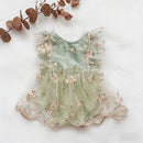 A sleeveless baby dress in pale mint green tulle with pink floral embroidery and pearl-like trim, laid flat on a white background with dried eucalyptus leaves in the corner, Obroi