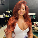 A woman with long, wavy coppery red hair sits in a salon chair wearing a white top and holding a purple phone. The background shows a dark salon interior with shelves and fixtures, Obroi