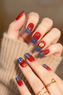 Nails with red and blue gradient design featuring apples and gold leaves, held by a person wearing a beige sweater, Obroi