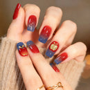 Nails with red and blue gradient design featuring apples and gold leaves, held by a person wearing a beige sweater, Obroi