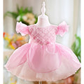 Pink children's dress on a mannequin with a blurred floral background, Obroi