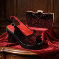 A black slingback platform sandal with red rhinestone embellishments and a matching red rhinestone clutch bag, displayed on a red velvet cloth over a wooden table, Obroi