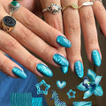 A close-up of manicured fingernails with a glossy metallic turquoise-blue leaf pattern, shown on a person's hands wearing multiple rings. Decorative nail art sample graphics appear at the bottom, Obroi
