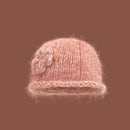 Pink knitted hat with a decorative flower on a brown background, Obroi 