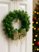 Christmas wreath with gold bow and ornaments on a white door, blurred Christmas tree in the background, Obroi