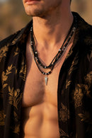 Man wearing a black floral shirt with a necklace, outdoors, Obroi