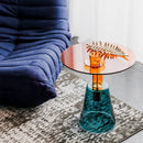 Small round table with a glass top and teal base next to a blue cushioned chair, Obroi