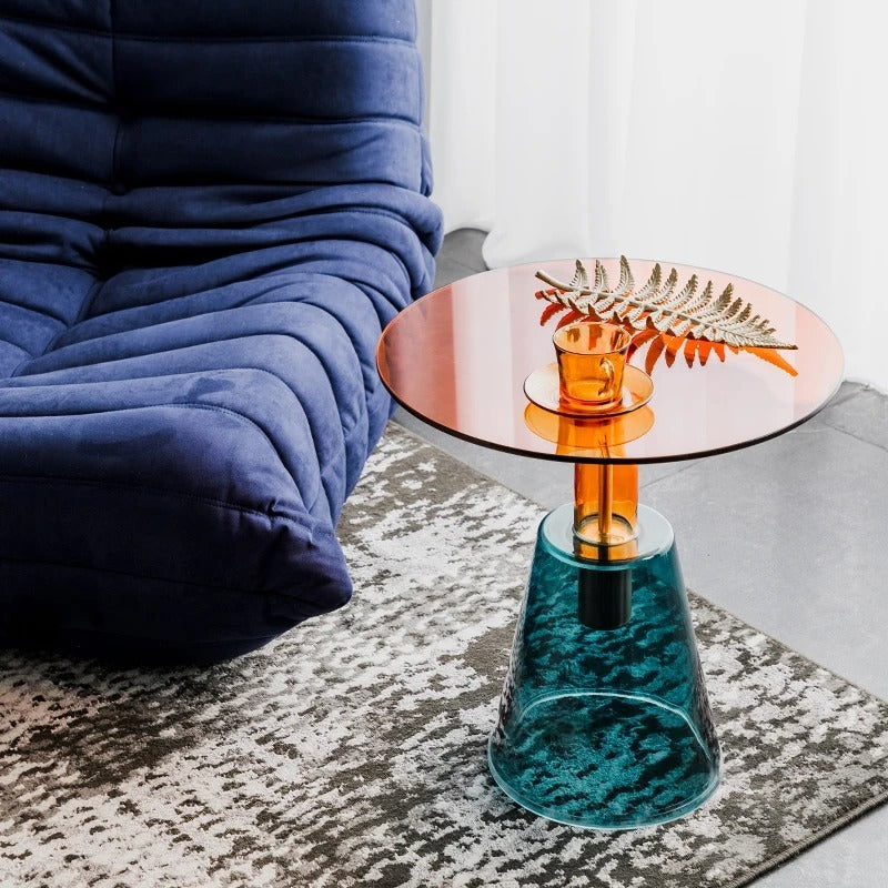Small round table with a glass top and teal base next to a blue cushioned chair, Obroi