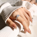 Close-up of a hand wearing a silver ring with a diamond, against a neutral background, Obroi