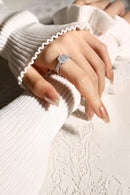 Close-up of a hand wearing a silver ring with a diamond, against a neutral background, Obroi