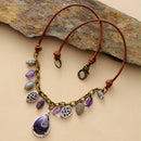 Bracelet with purple and gray beads on a brown leather cord against a stone background, Obroi