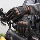 Person wearing black and brown motorcycle gloves on a motorcycle with Obroi branding.