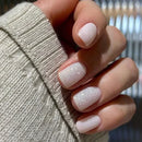 Close-up of a hand with pink glittery nails wearing a beige sweater, Obroi