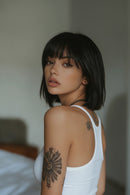 Woman with short black hair and tattoos on her arms wearing a white tank top, Obroi