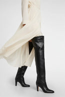 Black knee-high boots worn with a white skirt on a light gray background, Obroi