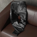 Black leather pants on a brown leather couch with a gray textured wall background, Obroi