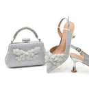 Silver clutch bag and high-heeled shoes with floral embellishments on a white background, Obroi