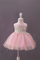 A pink children's party dress displayed on a white mannequin against a dark gray background. The dress features a sleeveless bodice with floral lace applique and a layered, fluffy tulle skirt, Obroi