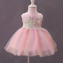 A pink children's party dress displayed on a white mannequin against a dark gray background. The dress features a sleeveless bodice with floral lace applique and a layered, fluffy tulle skirt, Obroi