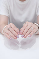 Close-up of hands with decorative nail art and rings, wearing a helmet in the background, Obroi