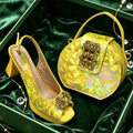 A yellow quilted slingback high-heel shoe and a matching yellow geometric handbag with jeweled embellishments, displayed in a green box lined with dark green velvet, Obroi