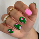 Hand with green nails featuring pink floral designs on a white background, Obroi
