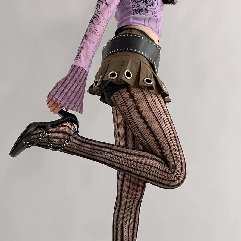 Person wearing patterned tights and a black skirt with grommets on a plain background