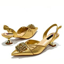 A pair of metallic gold slingback pointed-toe pumps with decorative crystal embellishments on the toe and mid-height metallic heels, shown on a clean white background, Obroi