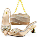 A women's formal shoe set with a matching rhinestone clutch bag, shown on a white background. The set includes a pair of pointed-toe mule heels in champagne satin with crystal embellishments, silver trim, and metallic gold cone heels, alongside a matching rectangular clutch with a yellow crystal bead handle, Obroi