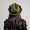 Person wearing a green fedora hat with a black band on a plain background, Obroi