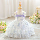 A toddler girl's floral print party dress displayed on a dress form mannequin. The dress features a white base with a light purple and green floral pattern, a lavender purple waistband with a bow, and a tiered ruffled tulle skirt, Obroi