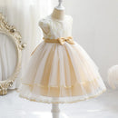 A toddler girl's formal party dress displayed on a mannequin. The dress features a cream lace bodice, a tiered tulle skirt in cream and pale gold, and a matching pale gold ribbon belt with a bow, Obroi