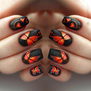 Nails with black and orange butterfly design held by a hand, Obroi