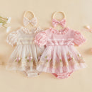 Two baby romper dresses displayed side by side on a warm beige background, each with a matching fabric bow headband. The left romper is cream/off-white with floral embroidery and lace, and the right romper is light pink with matching floral embroidery and lace, Obroi