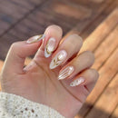 Hand with decorative nail art featuring gold and white designs against a blurred natural background, Obroi