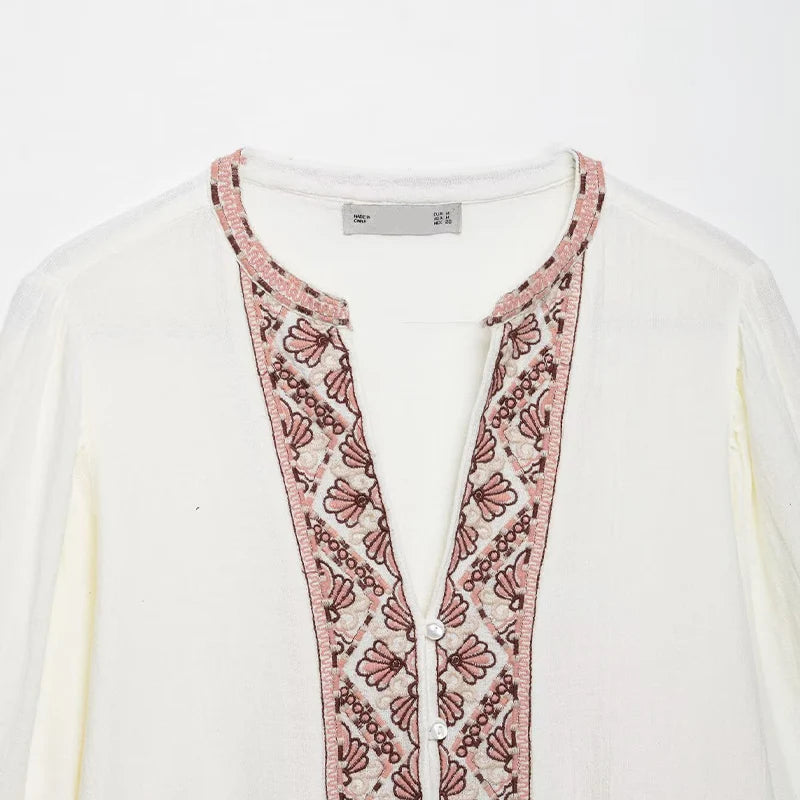 White cardigan with pink floral embroidery on a white background